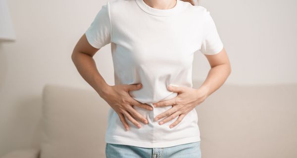 Junge Frau, fasst sich an den Bauch.