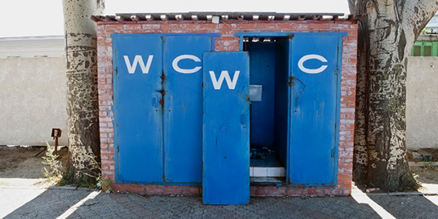 Blau gestrichene Toilettentüren, eine aus den Angeln gebrochen, gemauertes Toilettenhäuschen