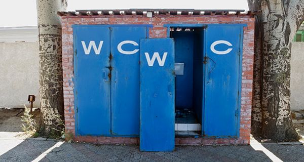 Blau gestrichene Toilettentüren, eine aus den Angeln gebrochen, gemauertes Toilettenhäuschen