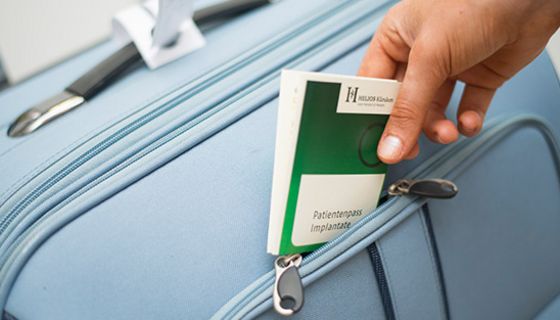 Eine Hand steckt einen Prothesenpass in einen Koffer.