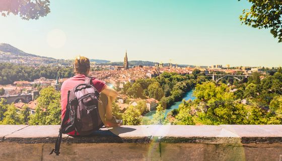 Ein junger Mann sitzt auf einer Mauer und schaut auf die Stadt Bern in der Schweiz.