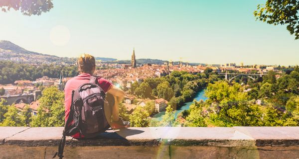Ein junger Mann sitzt auf einer Mauer und schaut auf die Stadt Bern in der Schweiz.