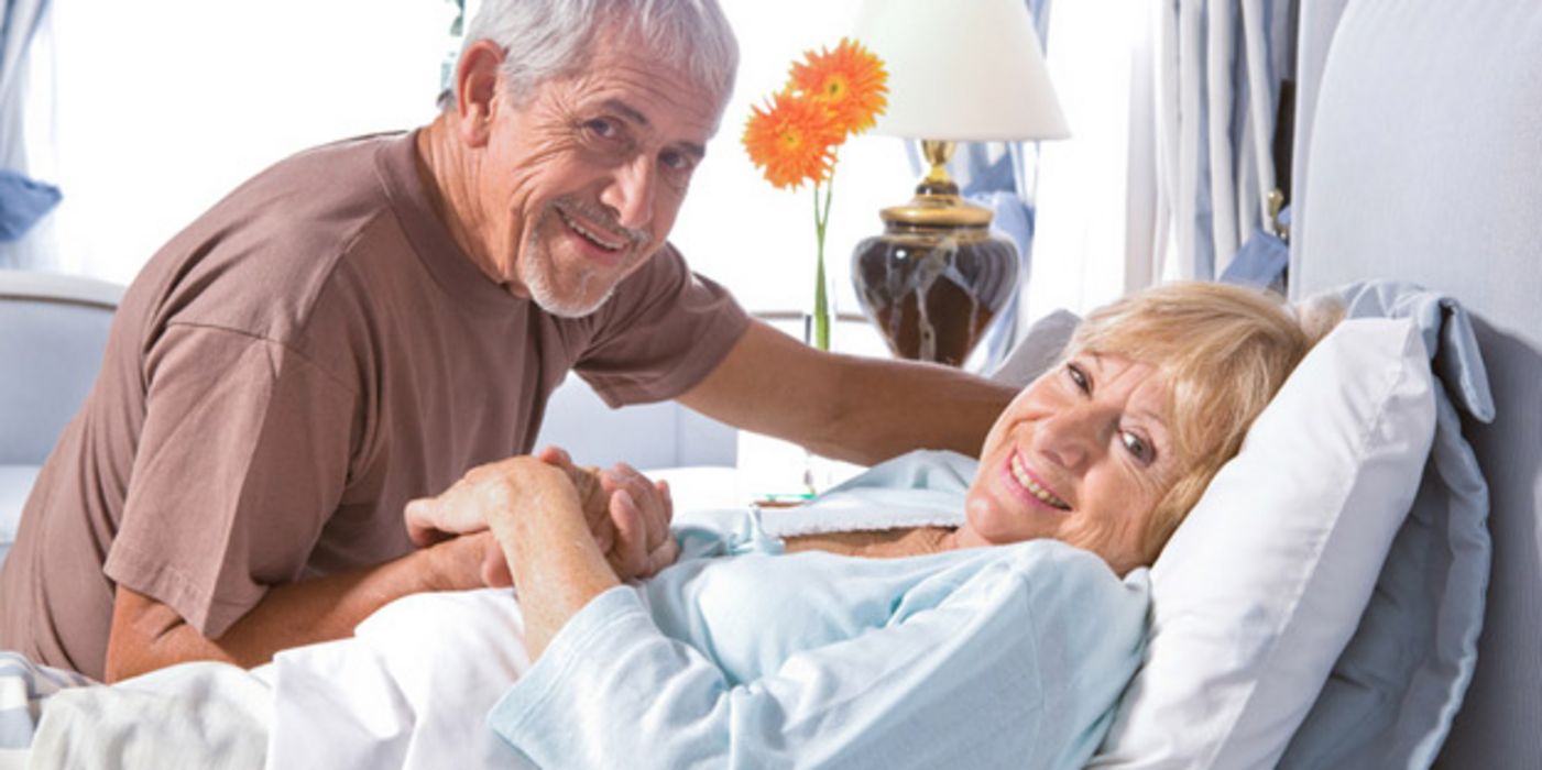 Seniorenpaar, Frau im Krankenbett bekommt Besuch von Mann