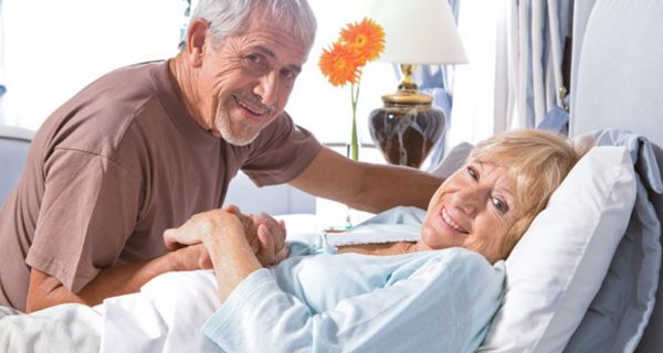 Seniorenpaar, Frau im Krankenbett bekommt Besuch von Mann