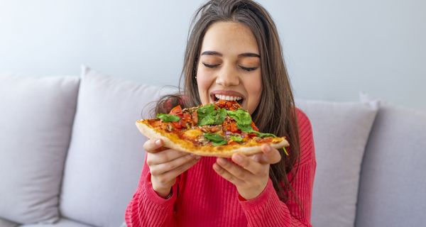 Junge Frau beißt in ein Stück Pizza.