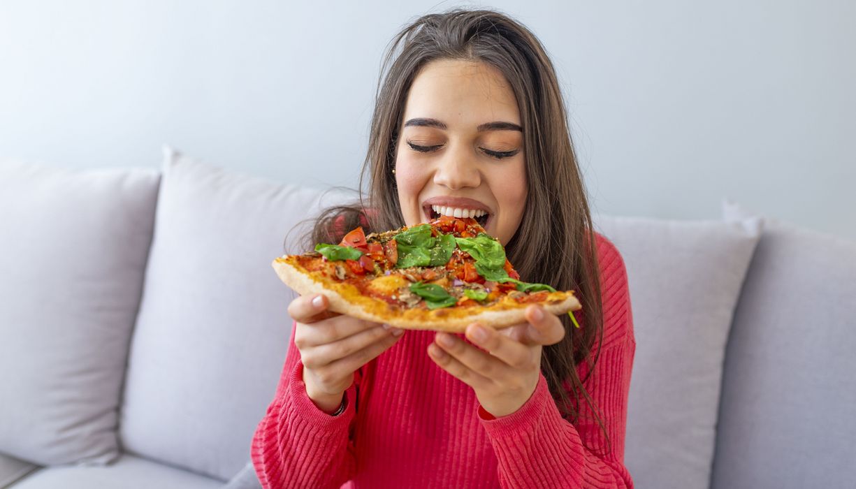 Junge Frau beißt in ein Stück Pizza.