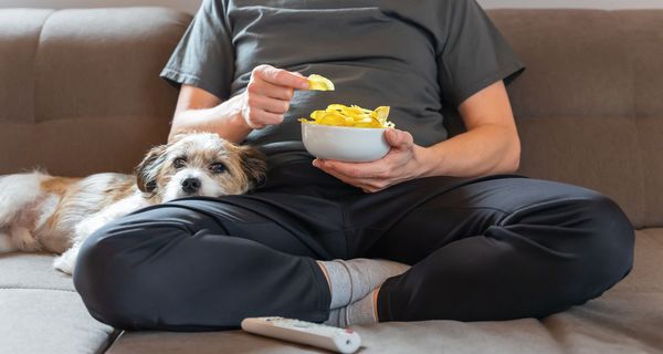 Frau, sitzt auf der Couch und isst Chips.