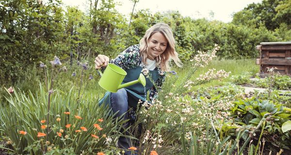 Frau, gießt Blumen in ihrem Garten.