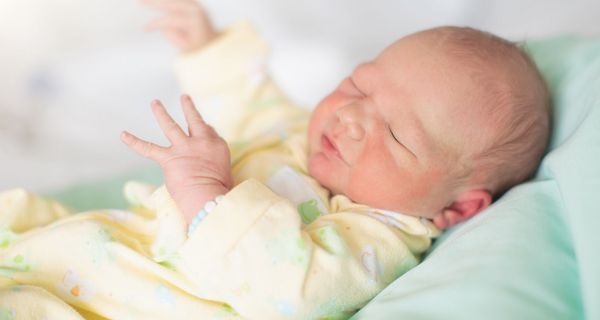 Neugeborenes mit geschlossenen Augen im Krankenhausbett.