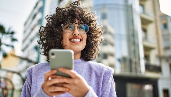 Junge Frau mit Brille und Locken schaut auf ihr Smartphone.