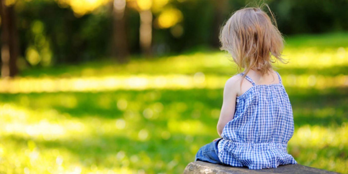 Kleines Mädchen sitzt schmollend im Garten