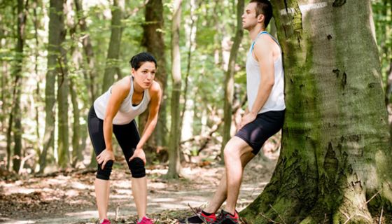 Joggerin und Jogger (ca. Mitte 20) in sommerlicher Sportkleidung verschnaufen im Laubwald