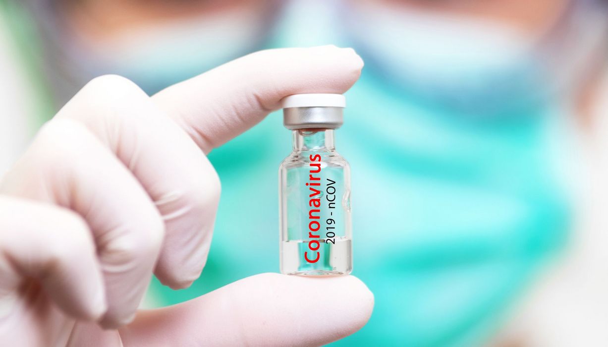 Forscher hält eine Dosis Corona-Impfstoff zwischen den Fingern.