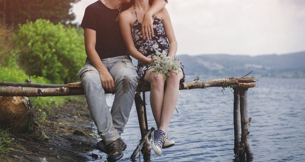 Zwei Jugendliche, sitzen Arm in Arm auf einer Brücke am See.