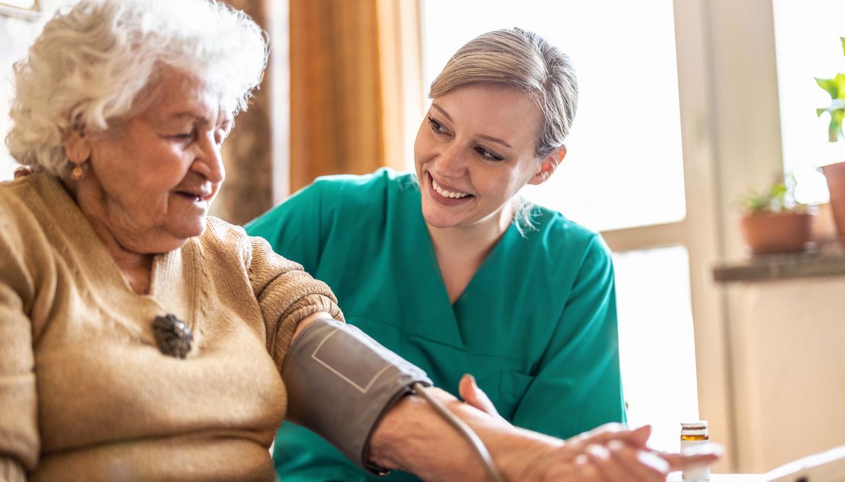 Freundliche Pflegekraft misst bei einer Seniorin den Blutdruck.