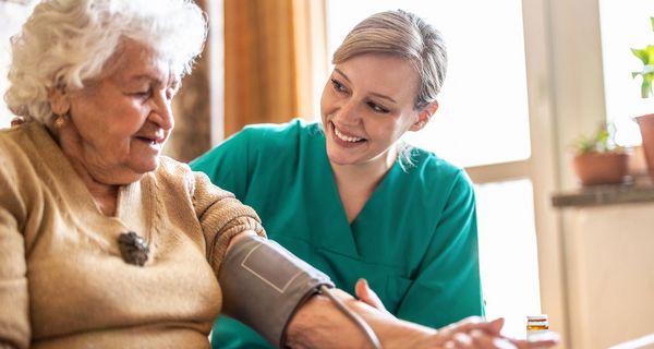 Freundliche Pflegekraft misst bei einer Seniorin den Blutdruck.