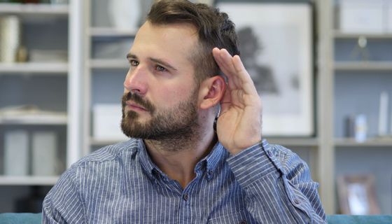 Junger Mann hält sich die Hand hinter das Ohr, um besser zu hören.