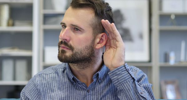 Junger Mann hält sich die Hand hinter das Ohr, um besser zu hören.