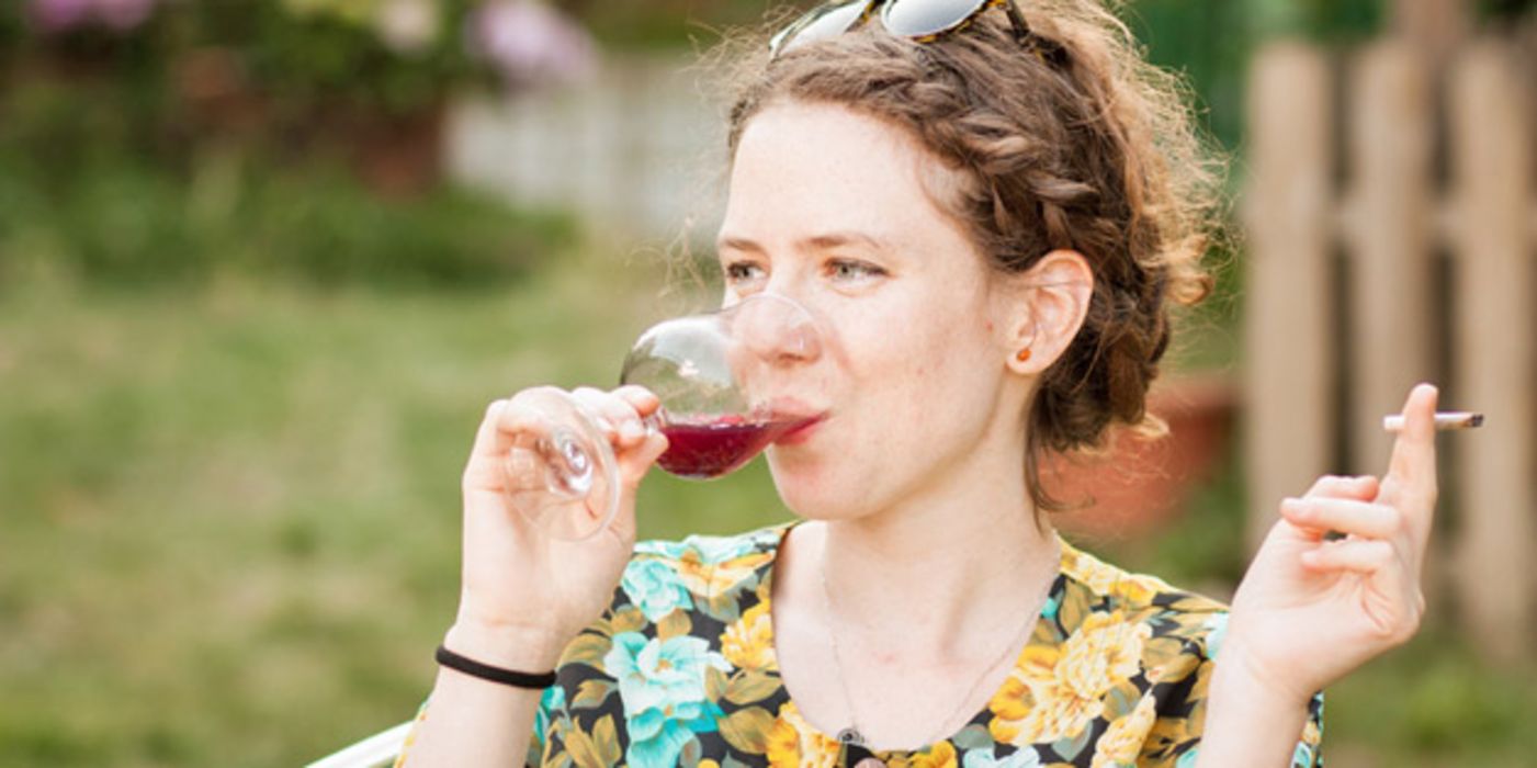 Junge dunkelhaarige Frau in bunter Bluse im Garten, rauchend, einen Rotwein trinkend