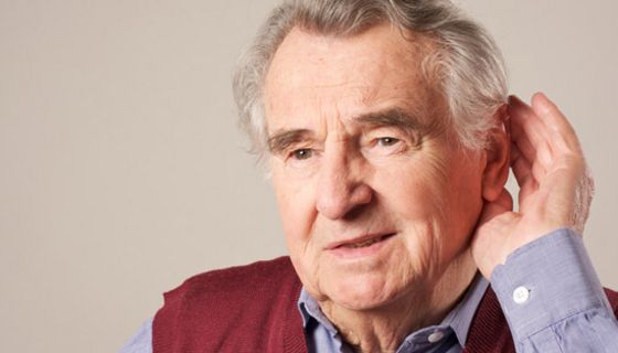 Älterer Mann, Nahaufnahme, hölt sich die Hand hinter das linke Ohr um besser zu hören