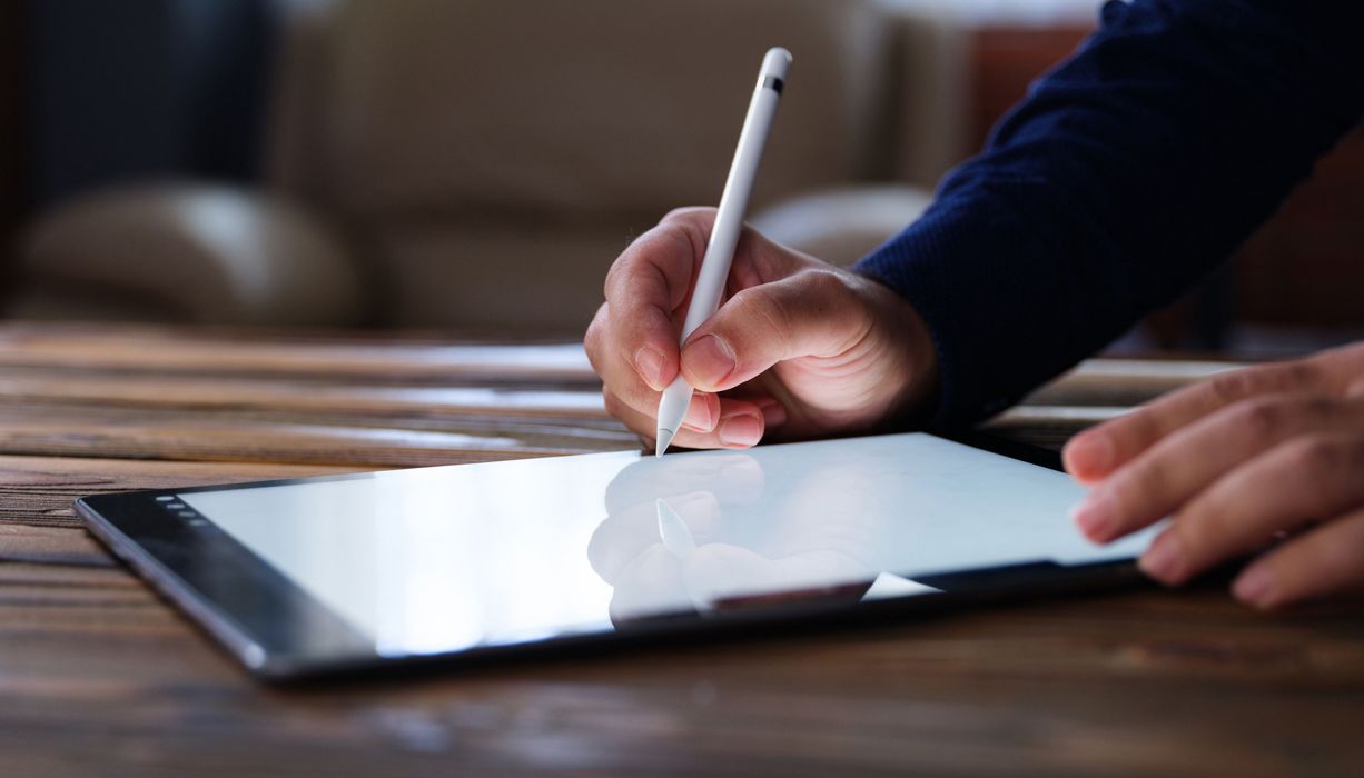 Hand mit Stift schreibt auf Tablet-Computer.