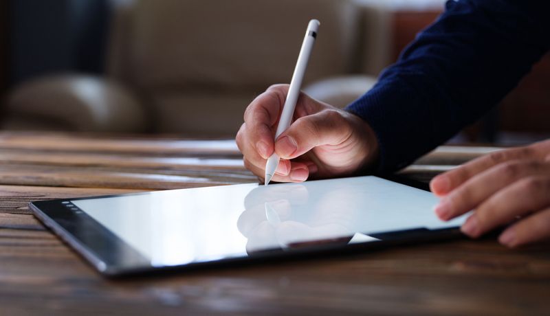 Hand mit Stift schreibt auf Tablet-Computer.