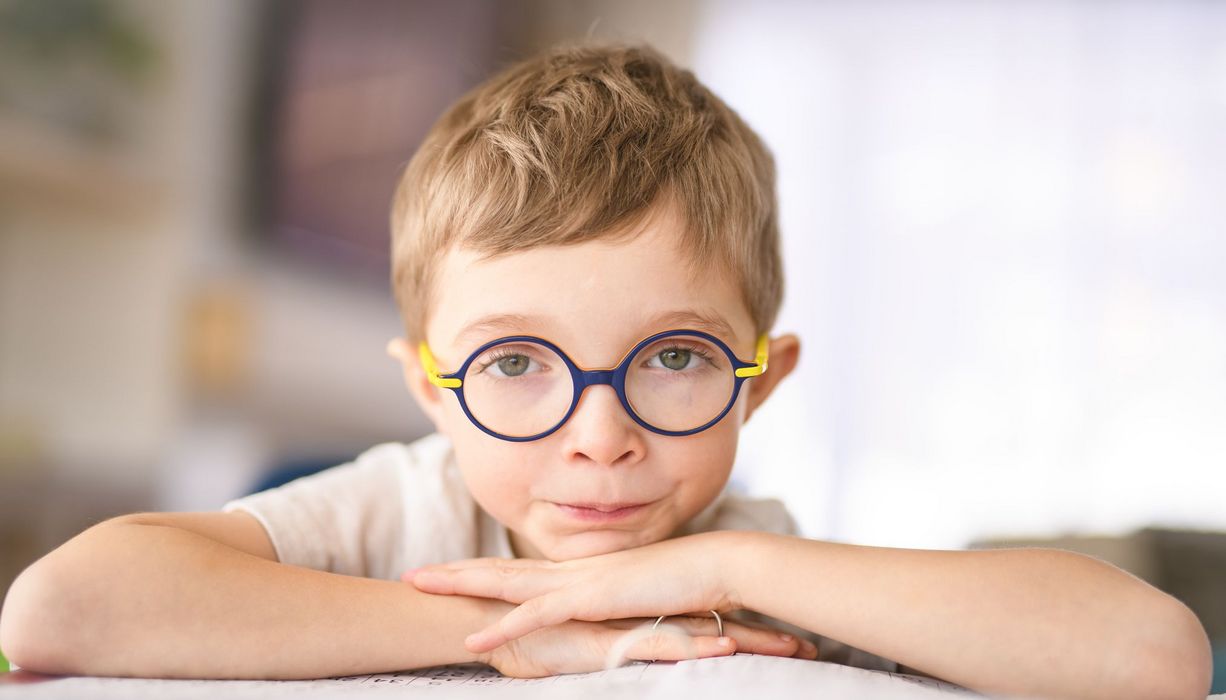 Junge mit Brille hat die Arme auf einem Ordner aufgestützt und blickt ernst in die Kamera.