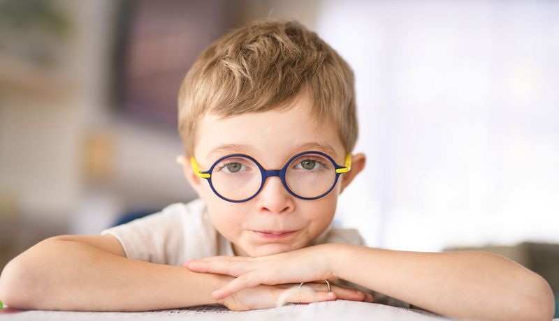 Junge mit Brille hat die Arme auf einem Ordner aufgestützt und blickt ernst in die Kamera.