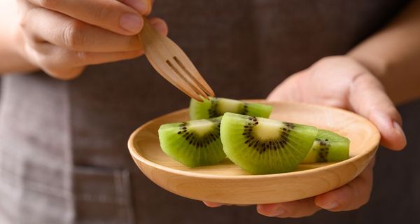 Jemand hält eine Schale mit aufgeschnittene Kiwi in einer Hand und piekst eine Scheibe auf.
