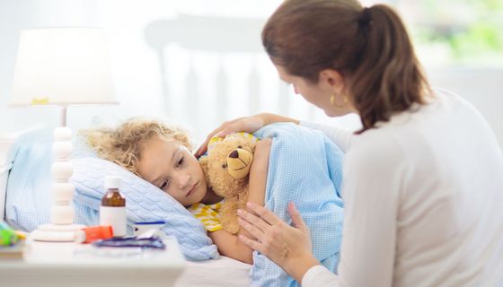 Mutter deckt krankes Kind im Bett zu.