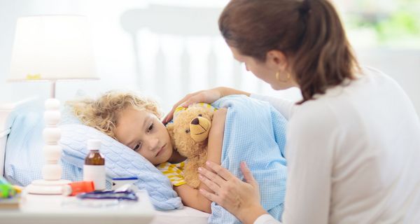 Mutter deckt krankes Kind im Bett zu.