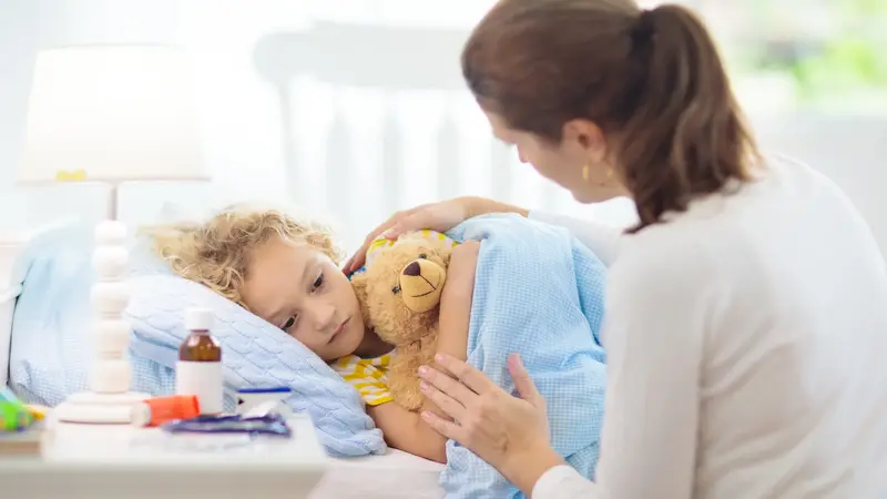 Mutter deckt krankes Kind im Bett zu.