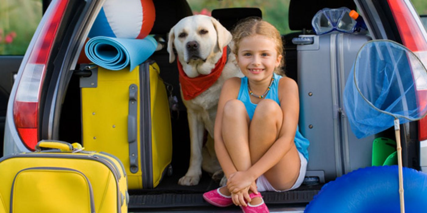 Mädchen und Hund sitzen in einem vollbepackten Autokofferraum