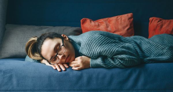 Junge Frau, liegt mit Brille auf der Couch und schläft.