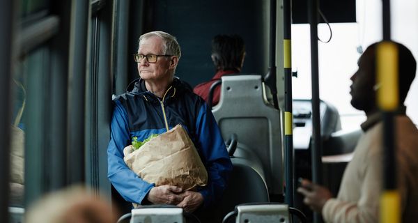 Älterer Mann ist mit Einkaufstüte im Bus.