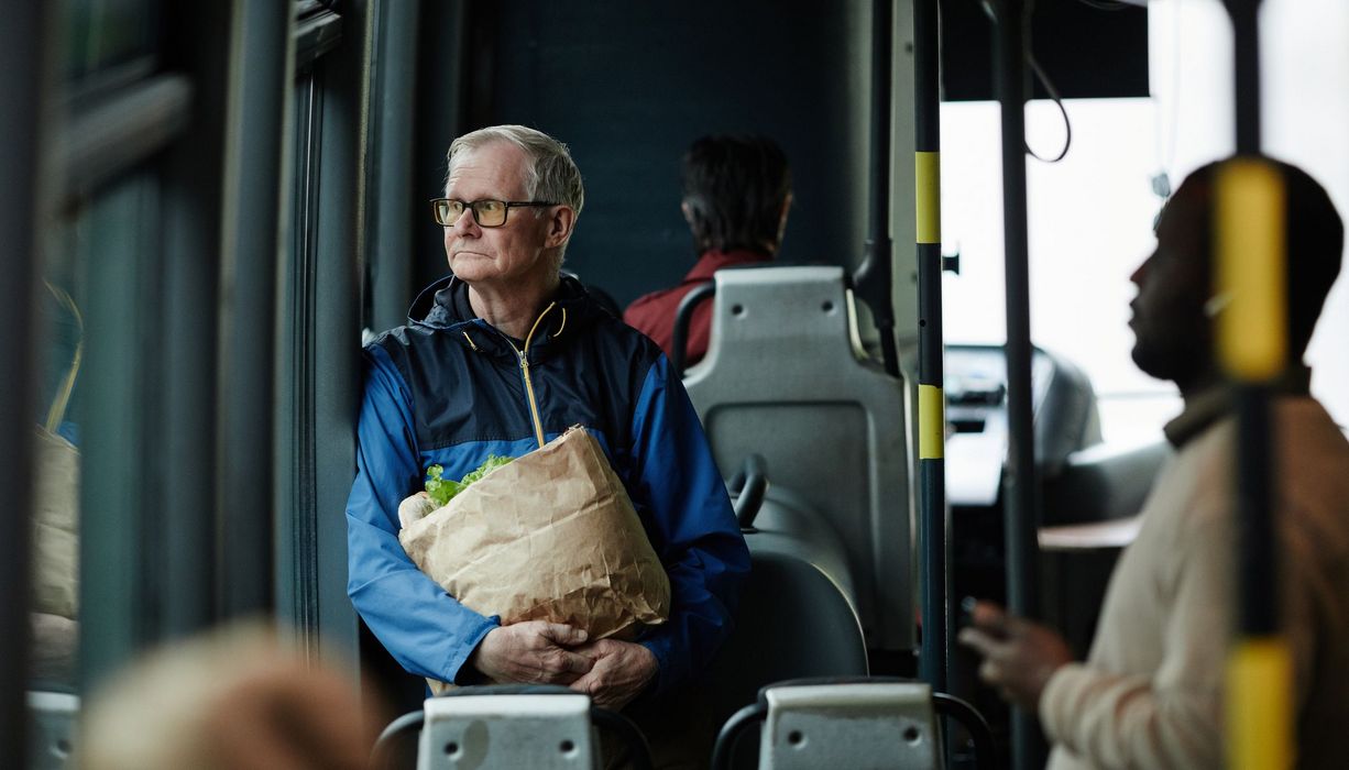 Älterer Mann ist mit Einkaufstüte im Bus.