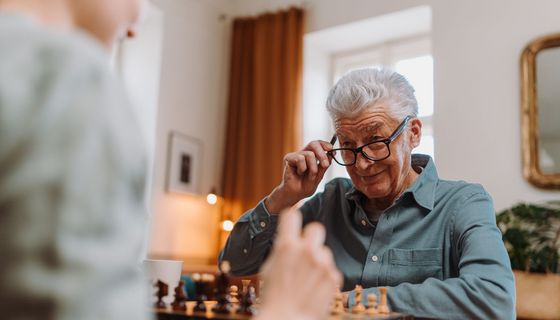 Älterer Mann sitzz mit Enkelin am Tisch und spielt Schach.