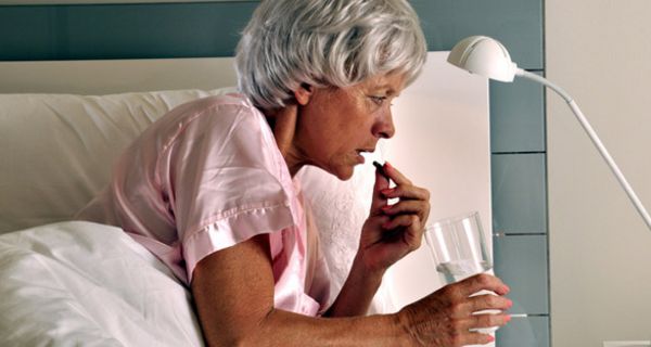 Frau um die 60 im Bett, rosa Nachthemd, graue, kurze Haare, bei Einnahme eines Medikaments