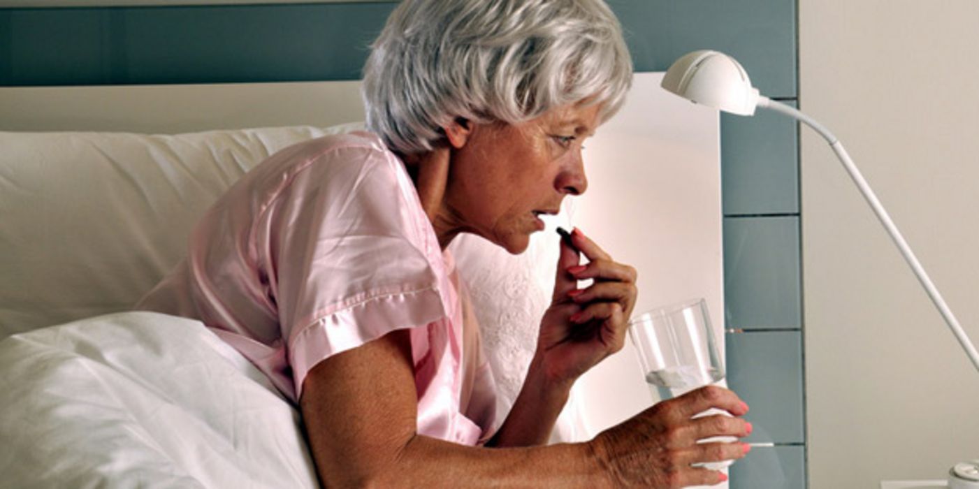 Frau um die 60 im Bett, rosa Nachthemd, graue, kurze Haare, bei Einnahme eines Medikaments