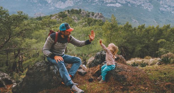 Vater und kleine Tochter, sitzen im Wald auf einem Fels und geben sich Highfive.