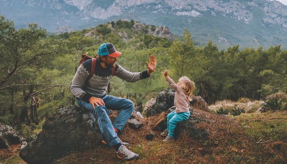 Vater und kleine Tochter, sitzen im Wald auf einem Fels und geben sich Highfive.