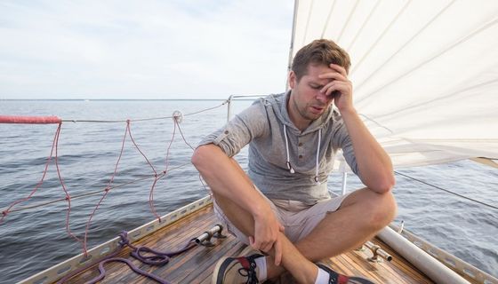 Mann, sitzt auf einem Boot und greift sich an den Kopf.