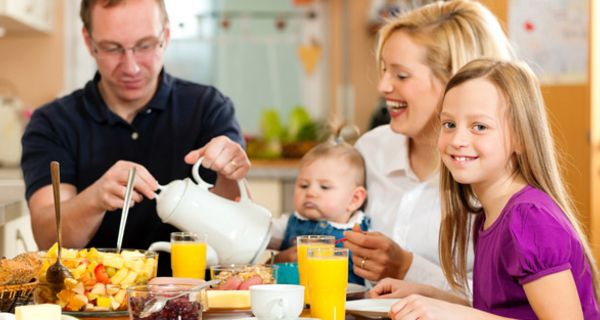 Mutter, Vater, Tochter (ca. 8 Jahre alt) und Baby beim vergnügten Frühstück, blonde Tochter im Vordergrund lächelt in die Kamera