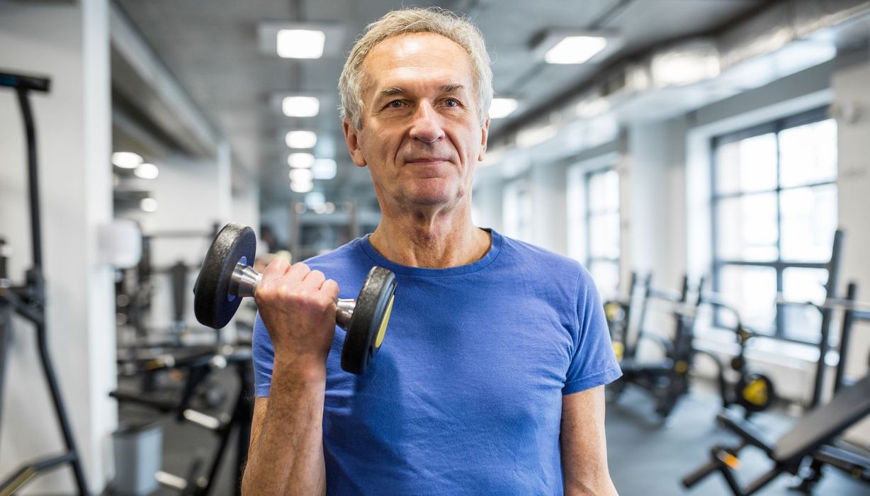 Senior trainiert mit einer Hantel im Fitnessstudio.