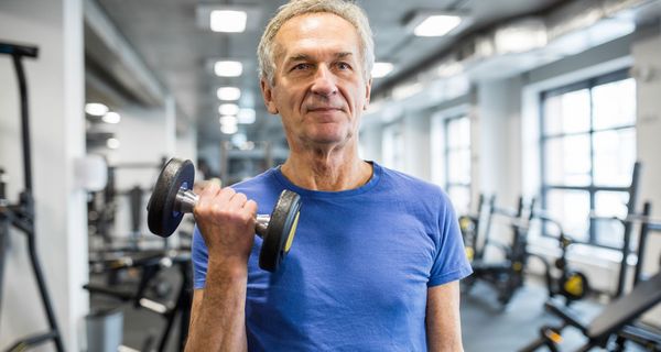 Senior trainiert mit einer Hantel im Fitnessstudio.