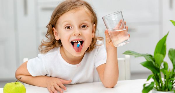 Kind nimmt eine Tablette mit einem Glas Wasser ein.