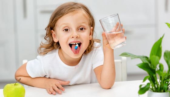 Kind nimmt eine Tablette mit einem Glas Wasser ein.