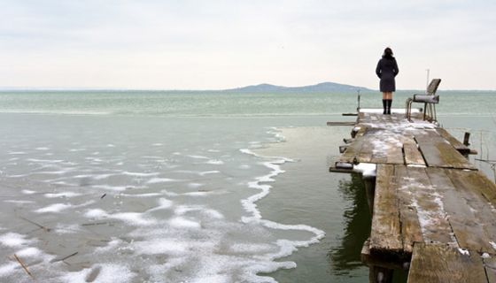 Mensch auf Steg blickt über einen See.