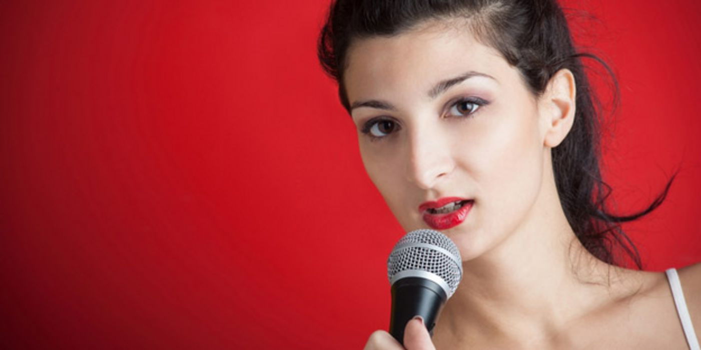 Junge dunkelhaarige Frau mit rot geschminkten Lippen singt in ein Mikrofon