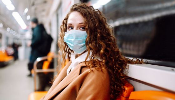 Junge Frau, sitzt in einer U-Bahn und trägt eine Maske.